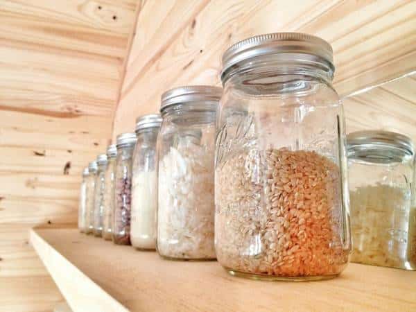 Rustic glass jars filled with pantry goods on wooden shelves.